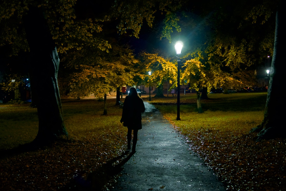 Female silhouette walking through a park in Bristol at night, lit be a streetlight